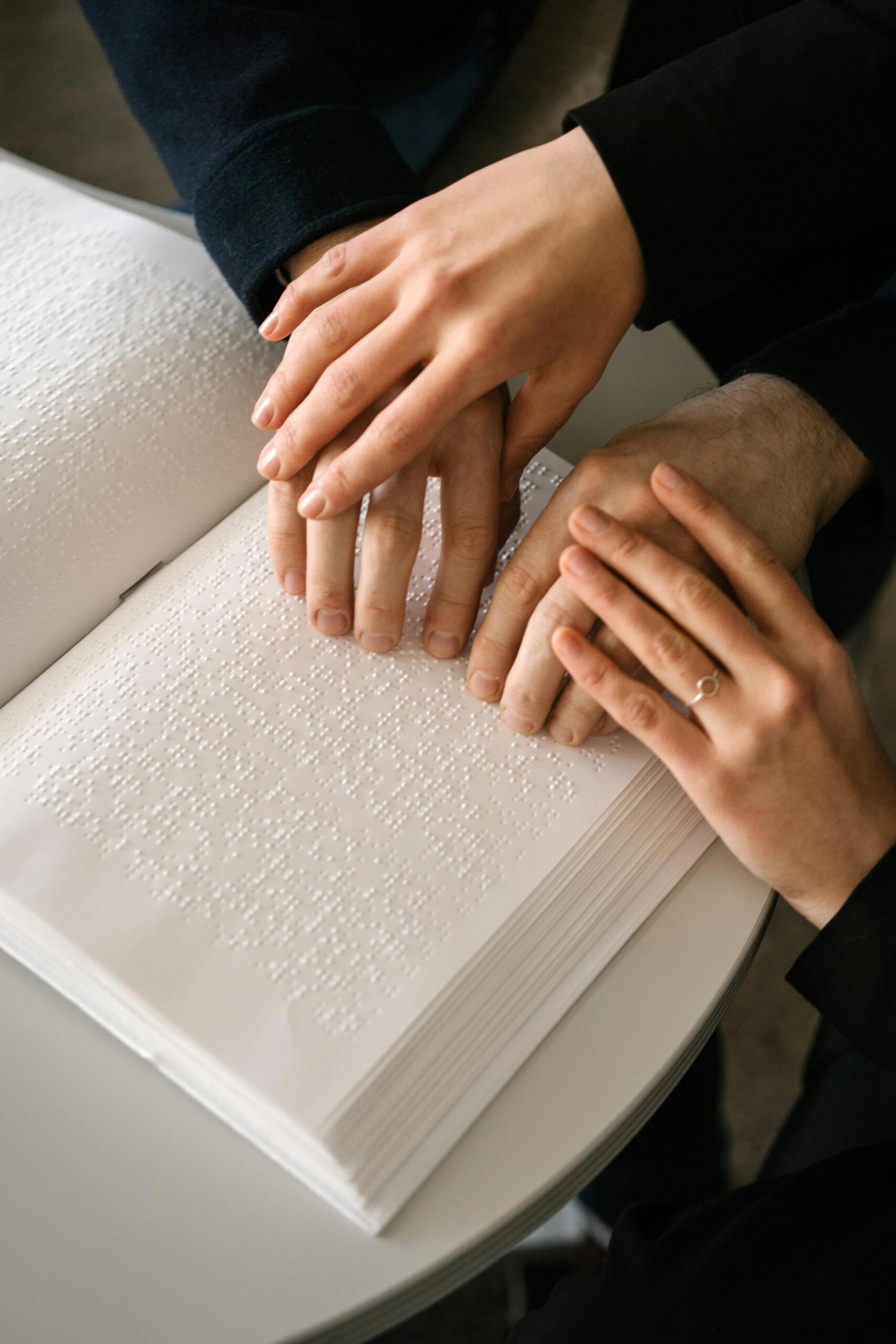 Close-up of hands reading a Braille book, symbolizing accessibility and learning.
